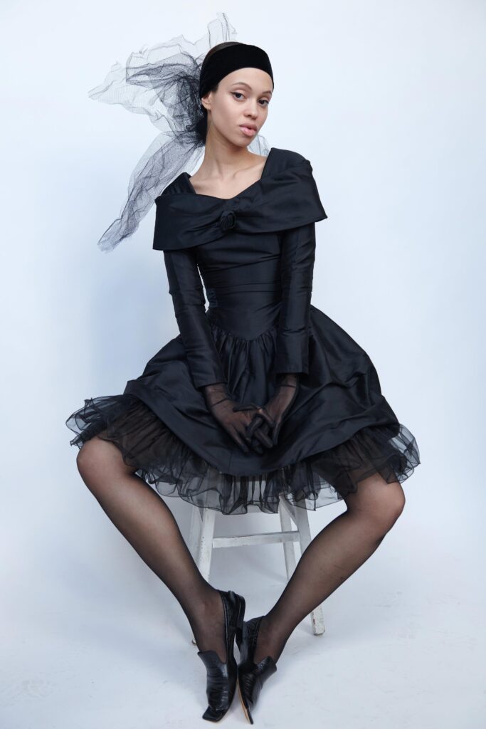 A fitted black silk dress with an off-shoulder design and tiered skirt.