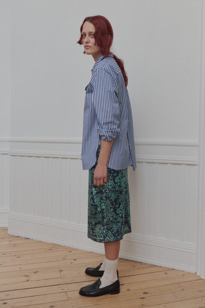 A relaxed blue striped shirt with long sleeves paired with a green floral skirt.