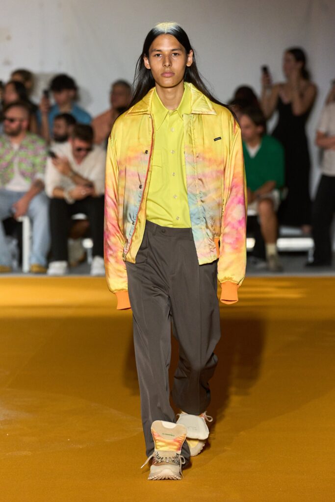 A relaxed multicolor cotton jacket with a collared neckline paired with gray pants.