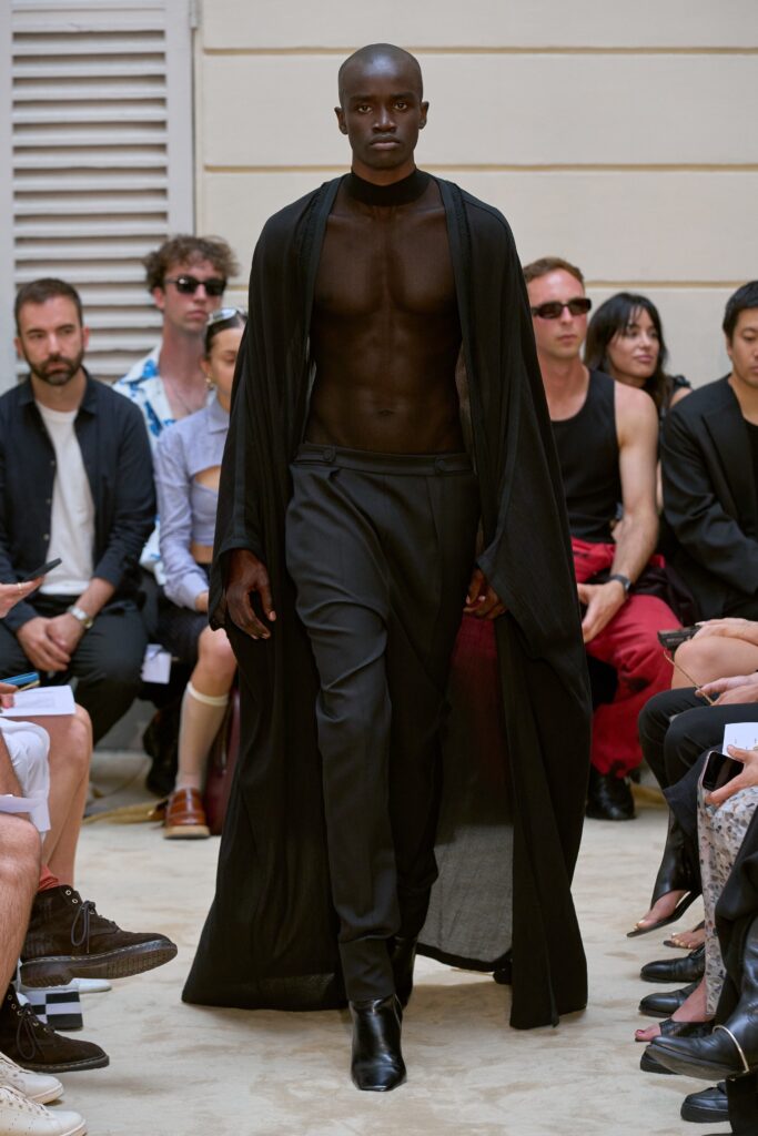 A fitted black silk coat with long sleeves and asymmetric design paired with sleek black pants.