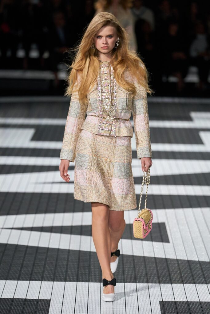 A fitted beige and pink tweed blazer with a collared neckline and a pleated skirt.