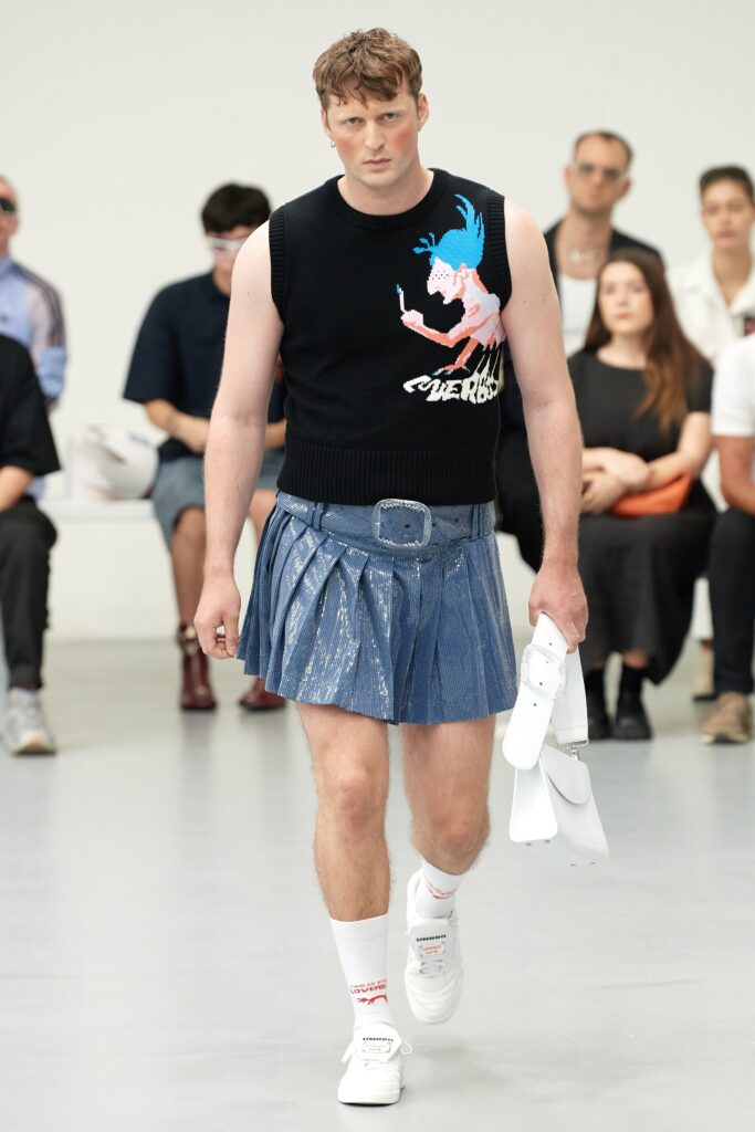 A fitted black sleeveless top with a printed design paired with a pleated blue denim skirt.