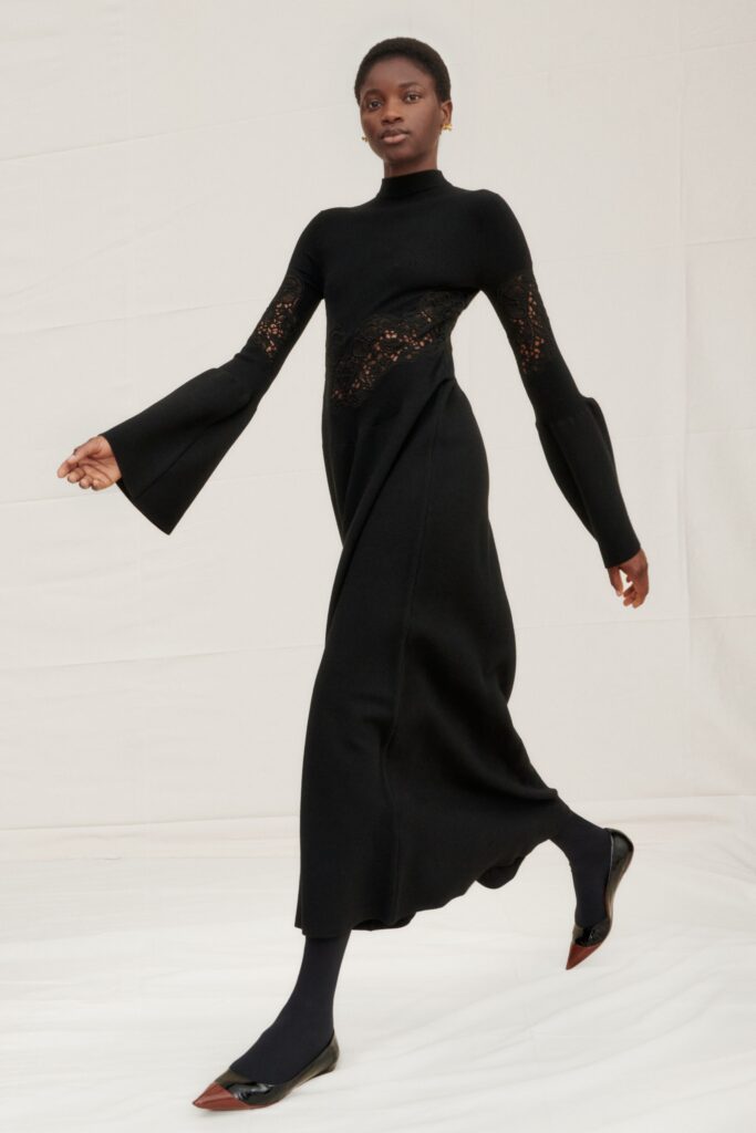 A fitted black knit dress with long sleeves, high neckline, and asymmetric design details.