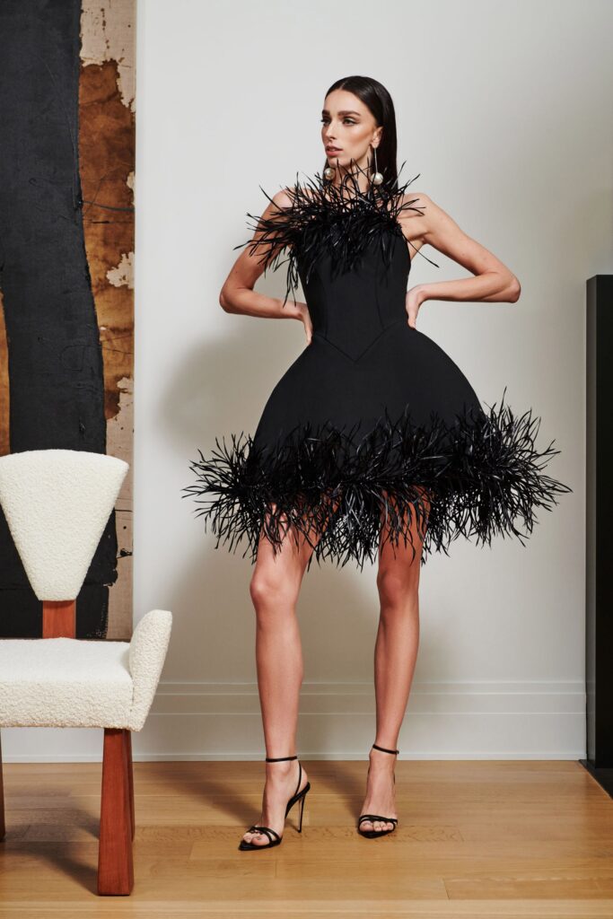 A fitted black silk sleeveless dress with an asymmetric silhouette and ruffled detailing.