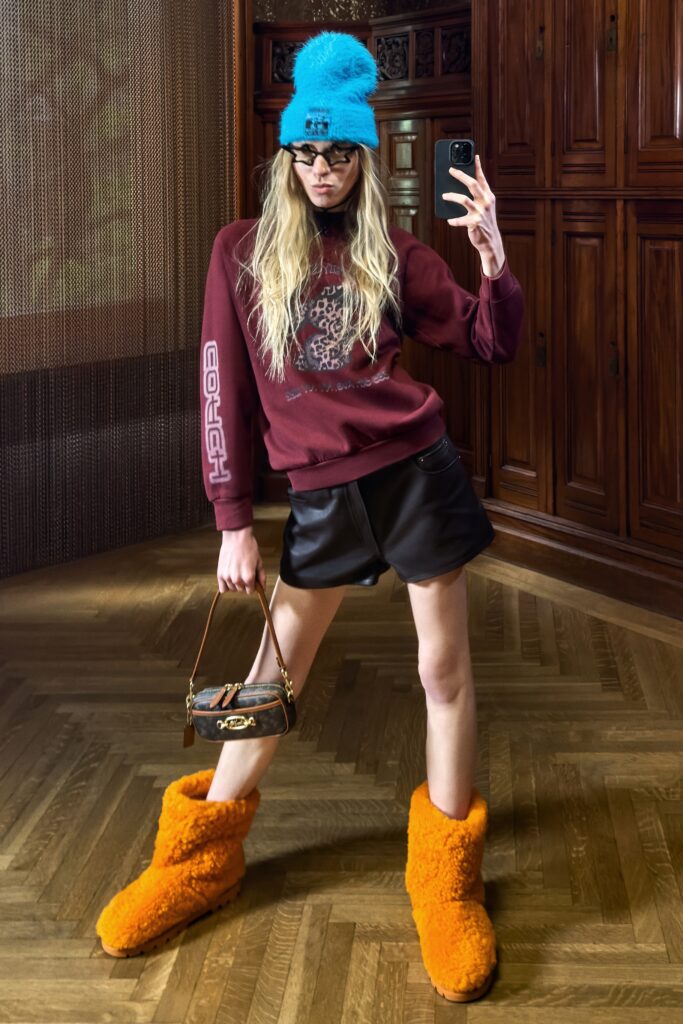 A relaxed red printed sweater paired with black leather shorts and orange boots.