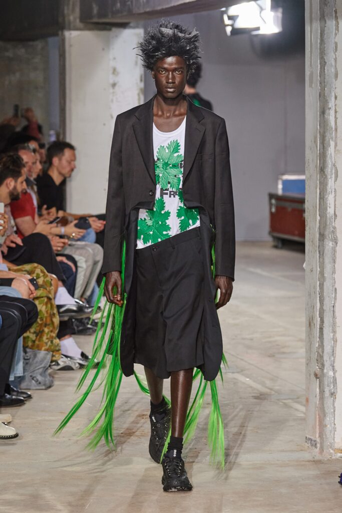 A relaxed black dress layered with a green graphic jacket featuring an asymmetric design.