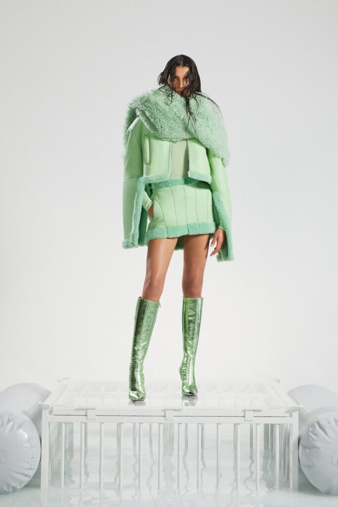 A fitted green fur jacket with a collared neckline paired with a zippered asymmetric skirt.