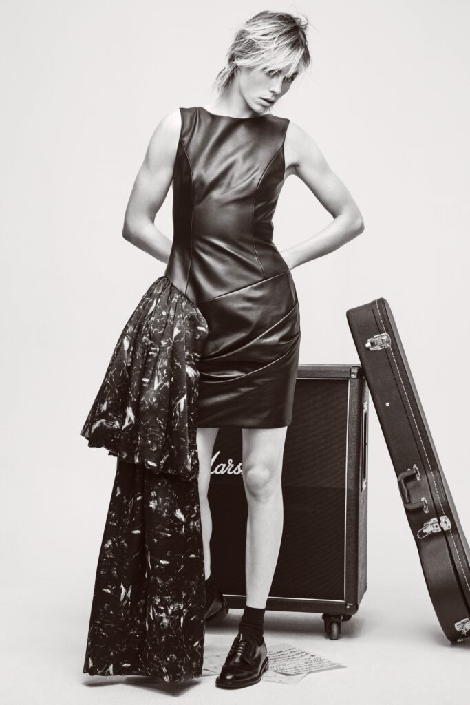 A fitted black leather sleeveless dress with a high neckline and draped design.