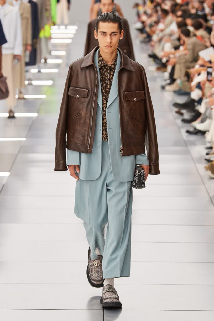 A fitted brown leather jacket paired with a blue suit featuring a collared shirt and layered design.