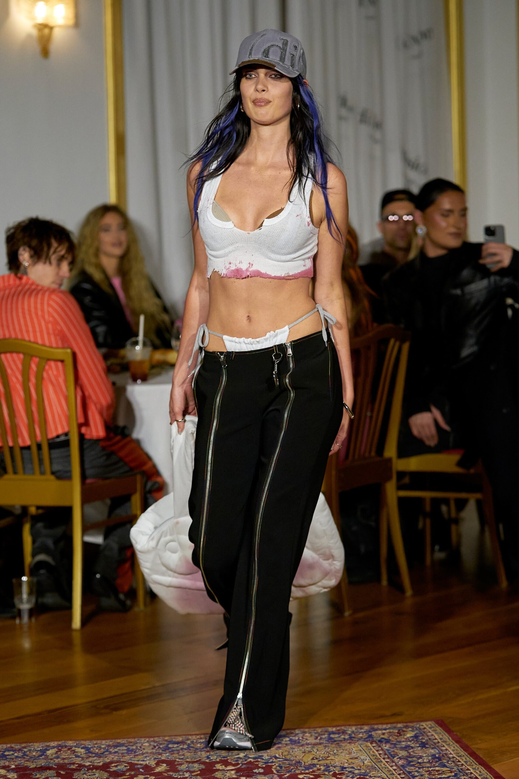 A fitted sleeveless white top paired with high-waisted black pants featuring zippered details.