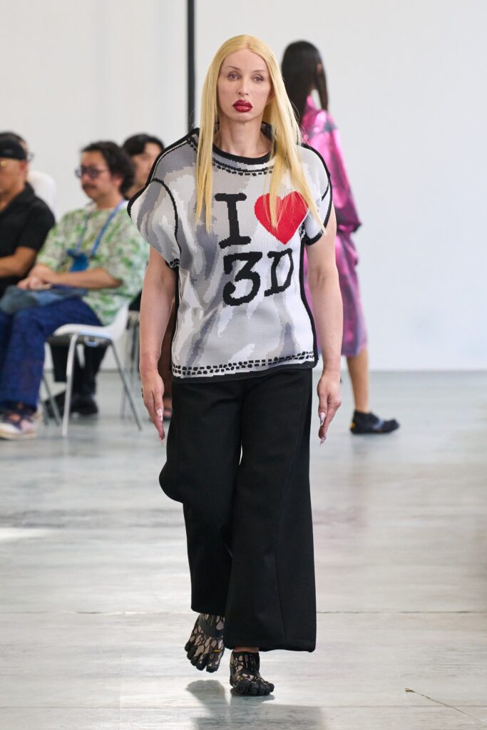 This ensemble features a relaxed-fit top adorned with a bold graphic print, complemented by wide-leg pants that create a striking silhouette. The playful contrast between the graphic elements and the flowing lines of the pants adds a dynamic touch to the overall look.