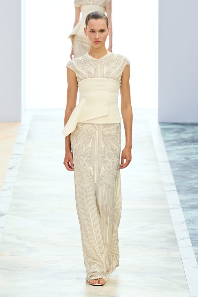 A fitted beige silk sleeveless dress with intricate embroidery and a high neckline.
