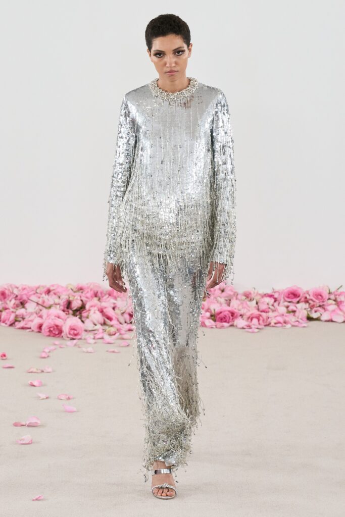 A fitted silver sequin dress with long sleeves, high neckline, and fringed detailing.
