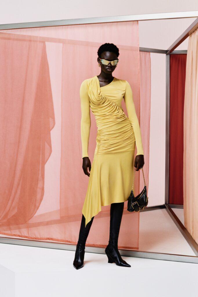 A fitted yellow silk dress with long sleeves, a V-neckline, and an asymmetric silhouette.
