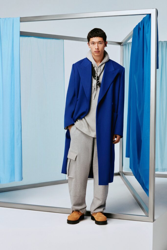 A relaxed blue coat paired with a hooded gray sweatshirt and relaxed gray pants.