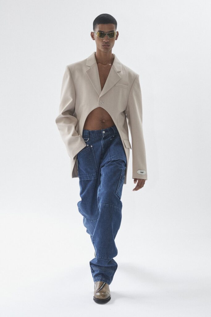 A relaxed beige jacket with long sleeves and a collared design paired with wide-leg blue pants.