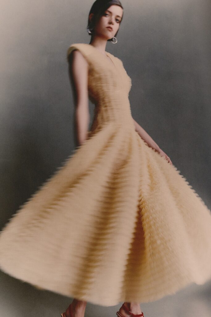 A fitted beige silk sleeveless dress with a V-neckline and pleated A-line silhouette.