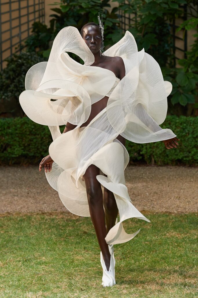 A fitted white silk sleeveless dress with a high neckline and layered asymmetric design.