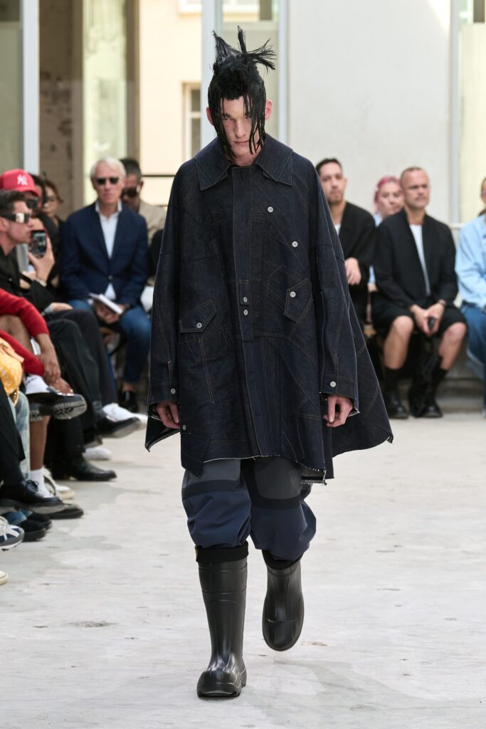 A relaxed black denim coat with long sleeves and an asymmetric design, paired with blue pants.