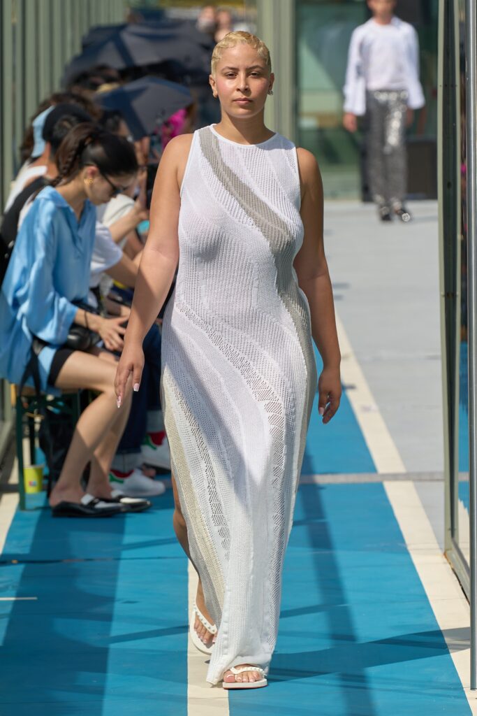 A fitted white sleeveless dress with a high neckline and sheer texture.