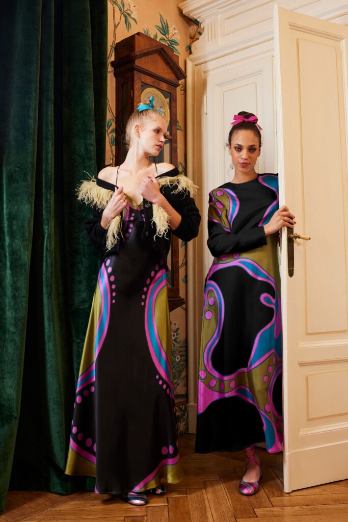 A fitted black silk dress with long sleeves, off-shoulder design, and vibrant printed details.