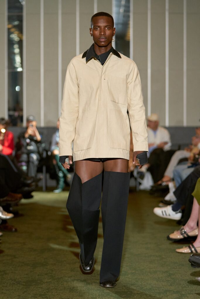 A relaxed beige cotton long-sleeve shirt with a collared neckline paired with black pants featuring an asymmetric design.