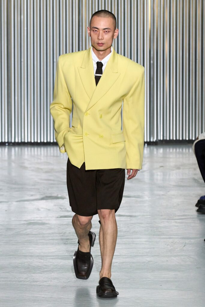 An oversized yellow blazer paired with brown shorts, featuring a collared neckline and buttoned detail.
