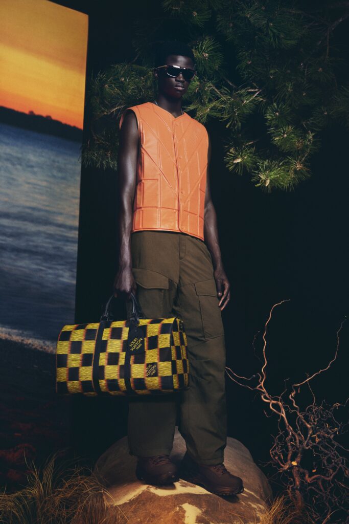 A fitted orange leather sleeveless vest paired with high-waisted green pants featuring an asymmetric design.