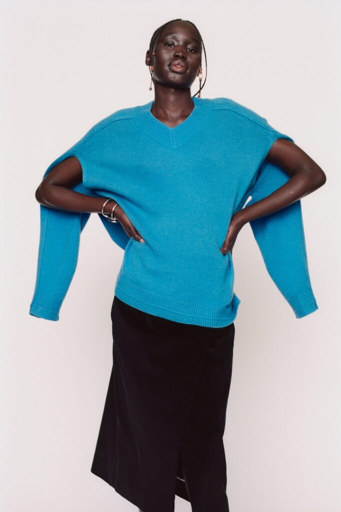 An oversized blue sweater with a V-neck and long sleeves paired with a black asymmetric skirt featuring a slit.