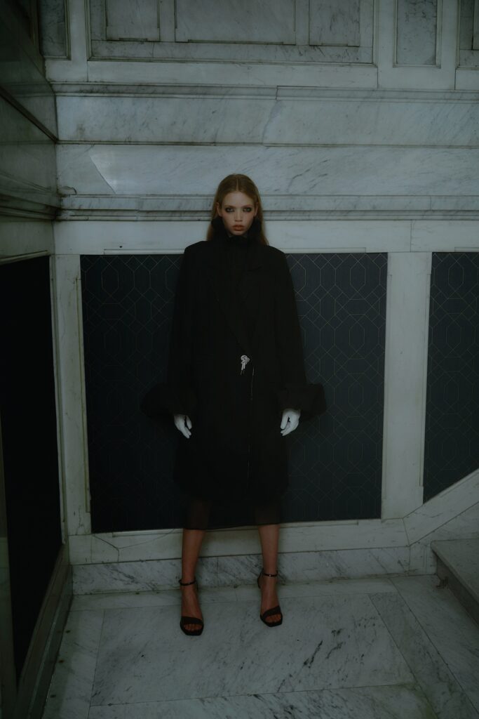 A relaxed black wool coat with long sleeves and an asymmetric design detail.