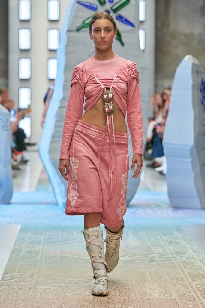 A fitted pink long-sleeve top with a cropped design and an embroidered asymmetric skirt.