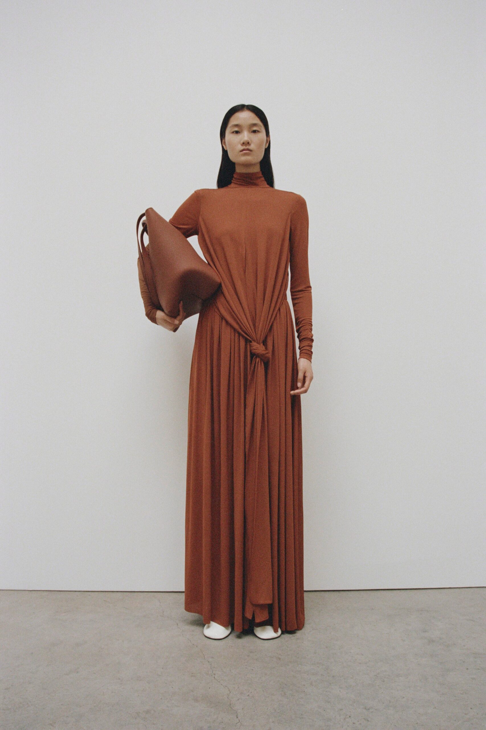 A fitted brown long-sleeve dress with a high neckline and draped design detail.
