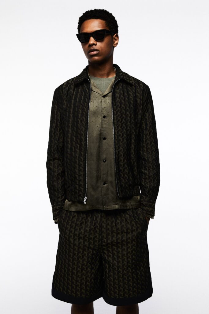 A relaxed fit black printed jacket paired with green shorts for a stylish summer look.