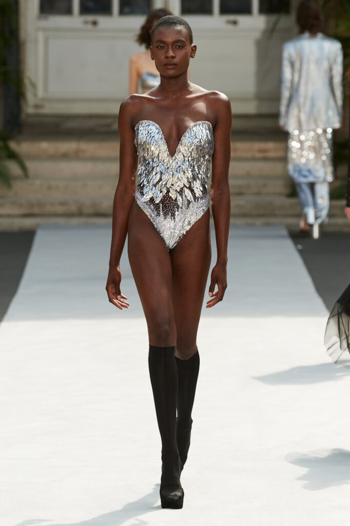 A fitted silver sequin bodysuit with a V-neckline and asymmetric design details.