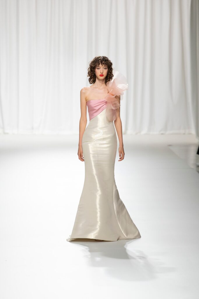 A fitted pink and cream silk gown with an off-shoulder design and flared silhouette.