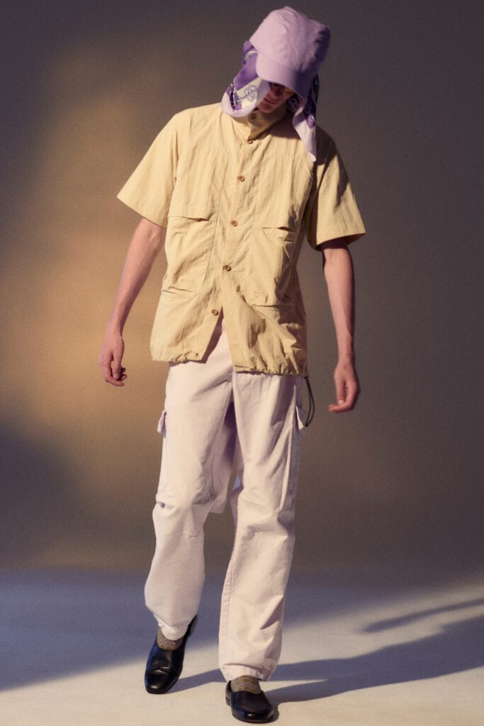 A relaxed beige cotton shirt with short sleeves and collared design paired with purple denim pants.