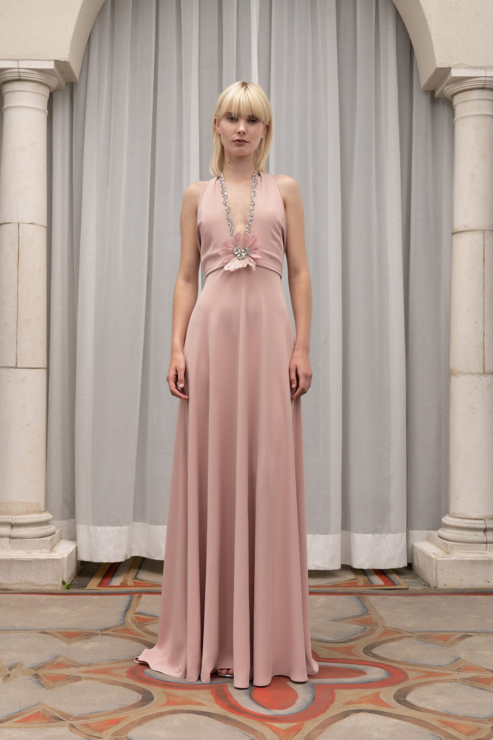 A fitted pink silk gown with a sleeveless design and V-neckline, featuring a flowing silhouette.