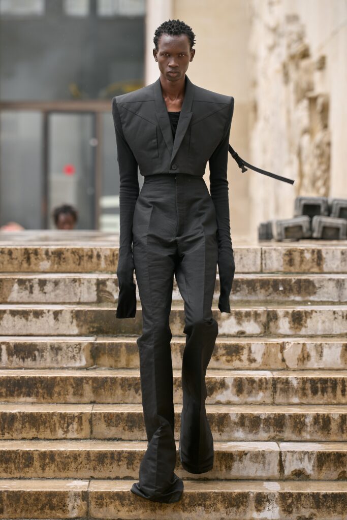 A fitted black jumpsuit with long sleeves, a collared neckline, and an asymmetric flared design.