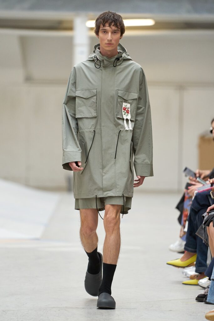 A relaxed green cotton coat with long sleeves and a hood, featuring a zippered detail.