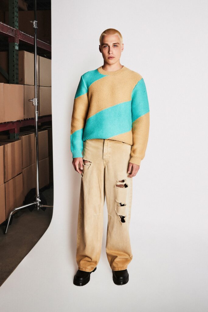 A relaxed long-sleeve beige and blue color-blocked sweater paired with relaxed beige pants.