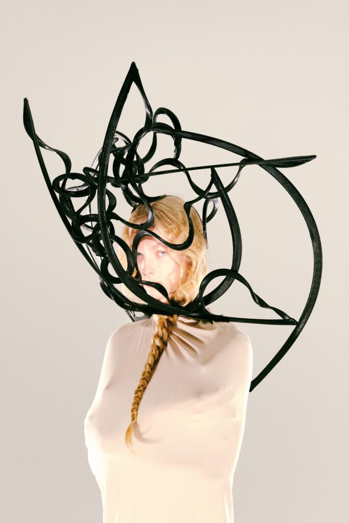 A fitted beige long-sleeve dress with a unique design and artistic headpiece.