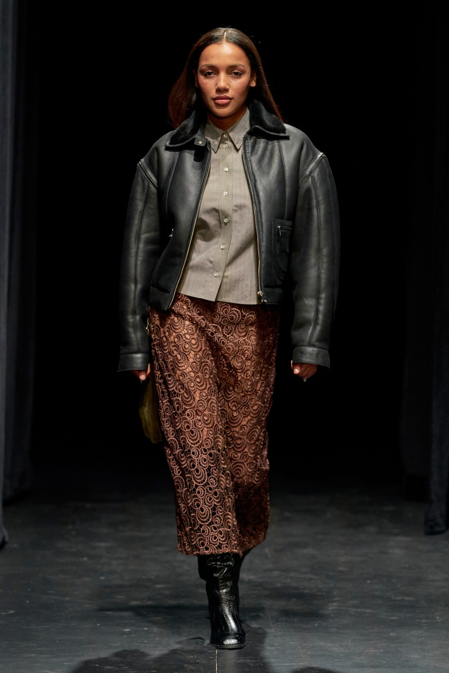 A relaxed black leather jacket paired with brown embroidered pants for a stylish look.