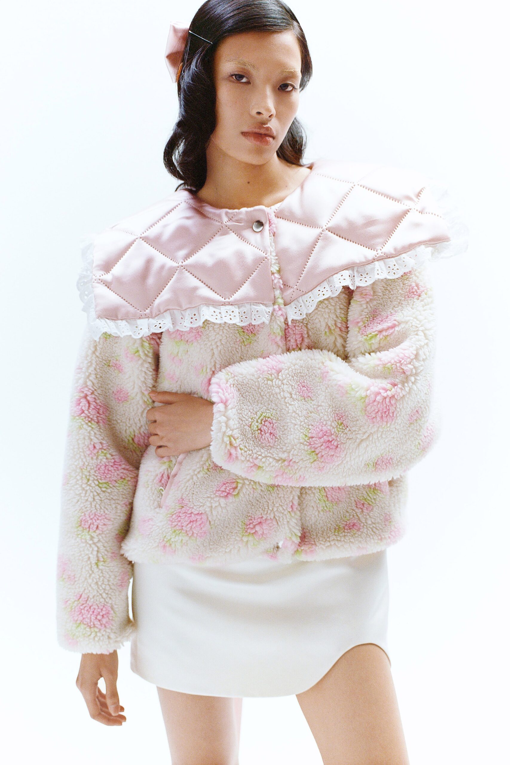 A relaxed pink faux-fur jacket with a collared neckline paired with a white skirt.