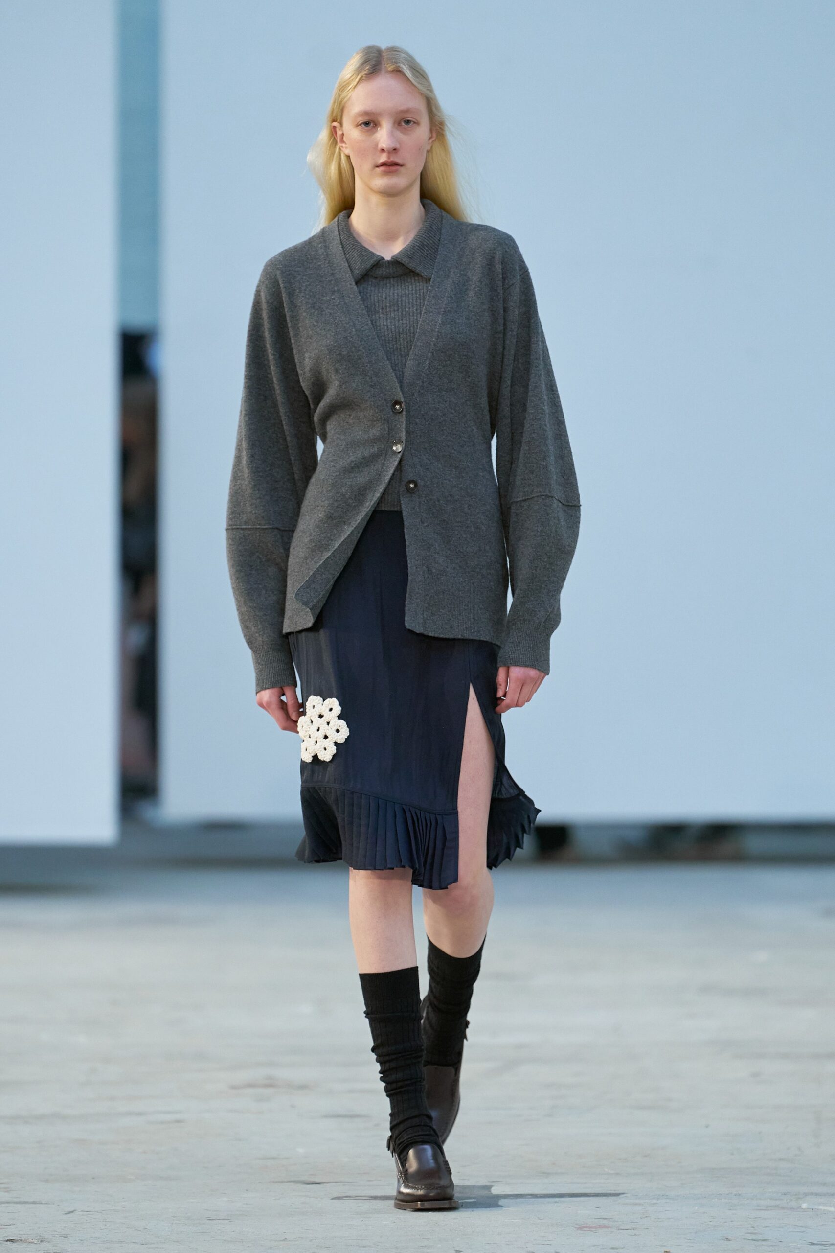 A relaxed gray wool cardigan layered over a pleated navy dress with a slit detail.