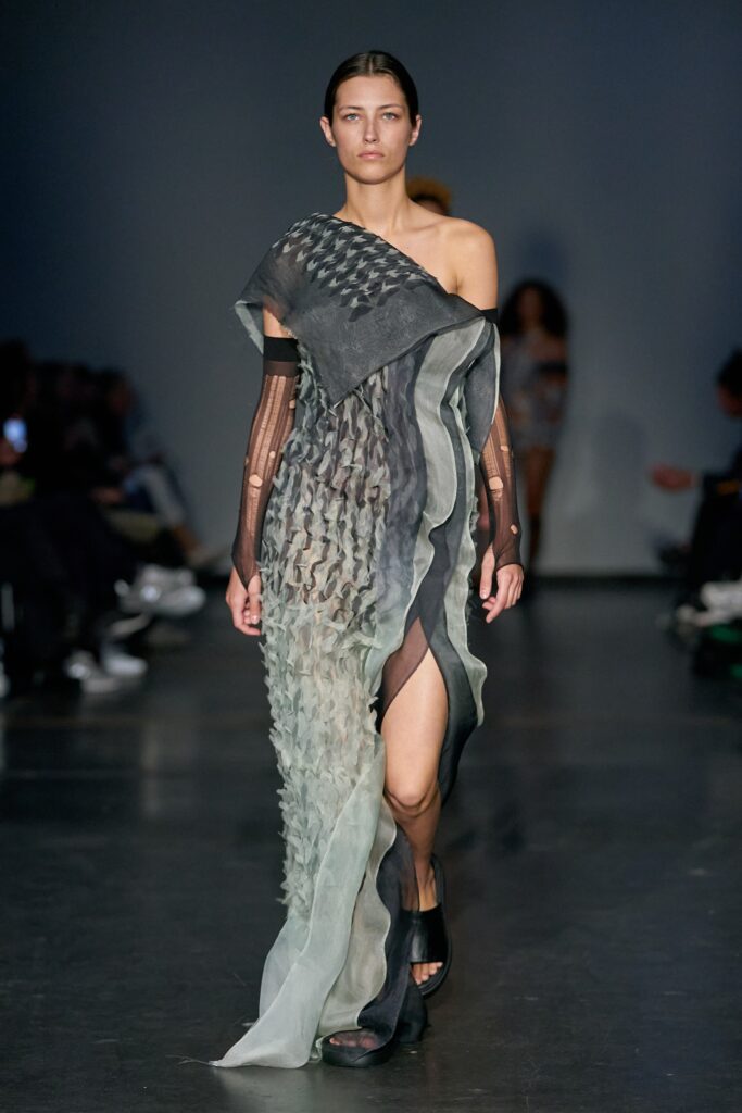 A fitted gray silk dress with an asymmetric design and layered texture featuring a slit.