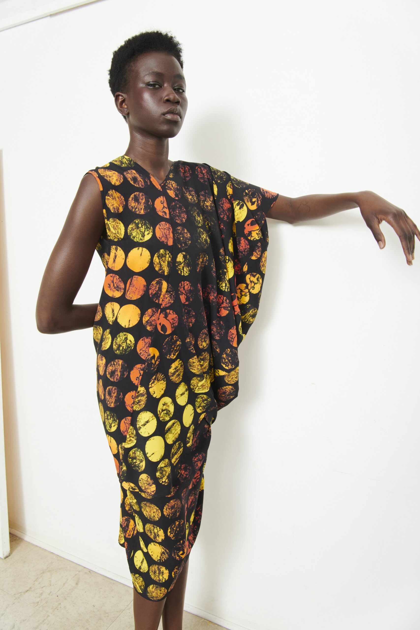 A relaxed sleeveless black dress with a V-neckline and asymmetric design featuring yellow and orange patterns.