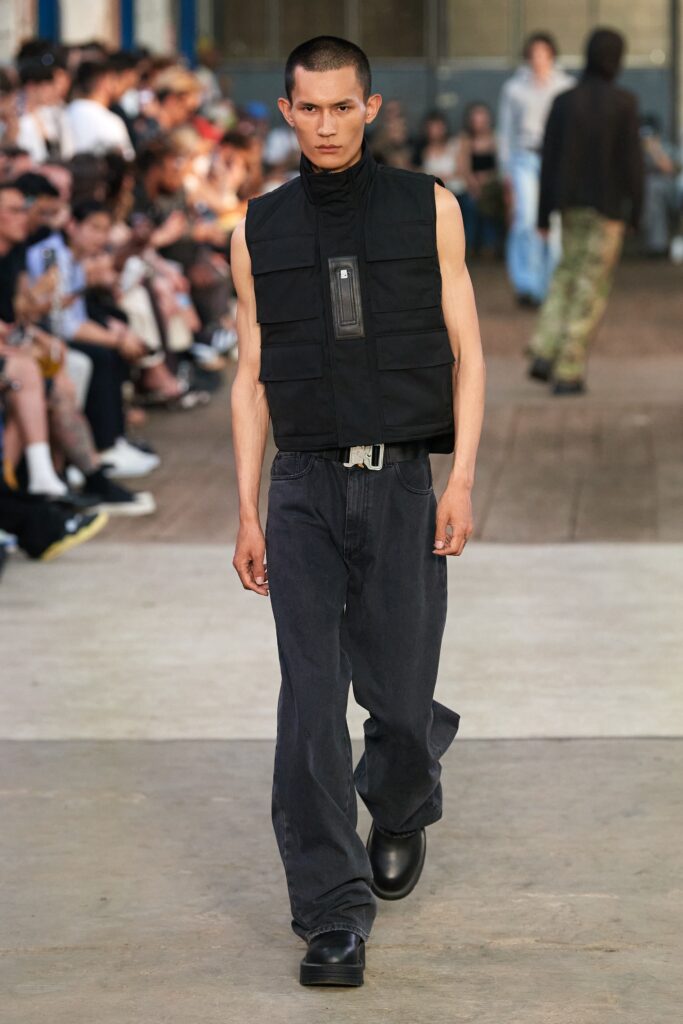 A relaxed black sleeveless vest with a high-neck and zippered detail, paired with loose-fitting pants.