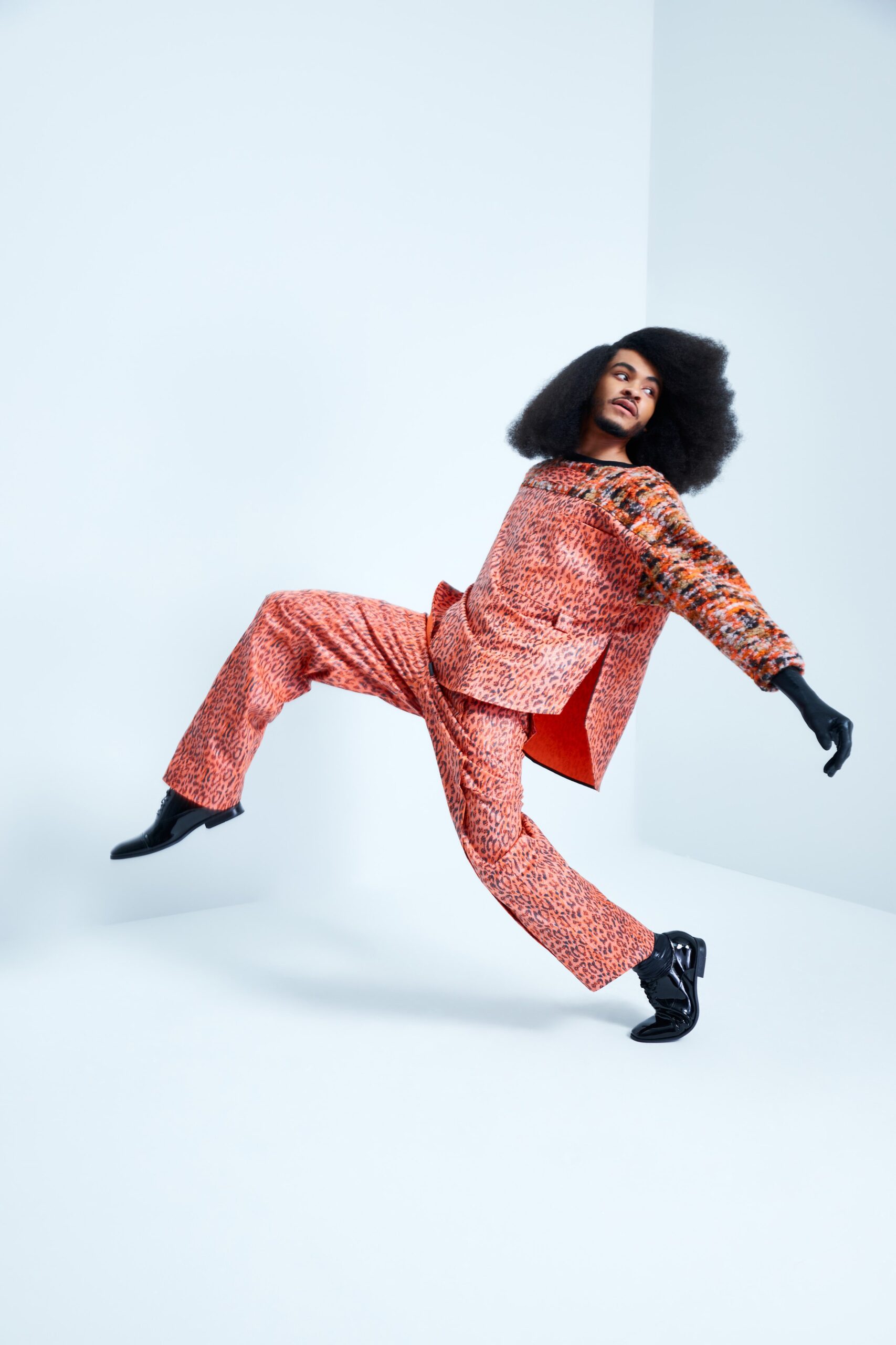 This ensemble features a relaxed top with long sleeves and a collared neckline, complemented by straight-leg pants. The vibrant orange fabric is adorned with an intricate print, creating a lively visual rhythm that enhances movement.