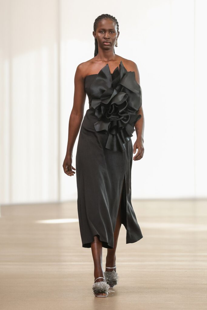 A fitted black silk sleeveless dress with an asymmetric design and pleated details.