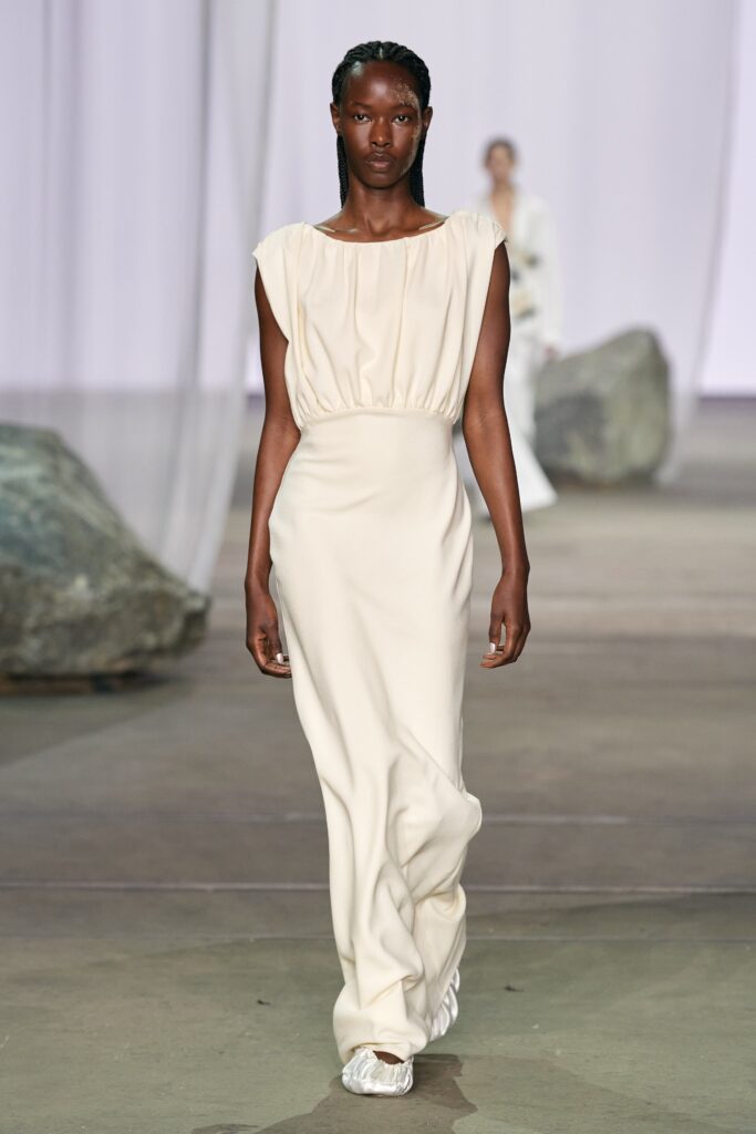 A fitted cream silk sleeveless dress with a high neckline and draped design.